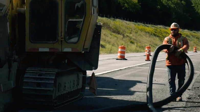 CAHill Tech. Construction worker follows vehicle with large pipe.